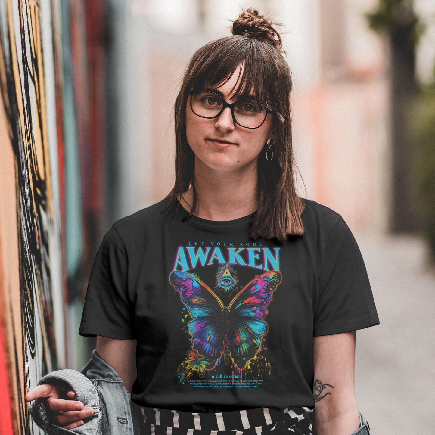 Person wearing a black t-shirt with a colorful butterfly graphic and 'Awaken' text, standing in an urban setting.