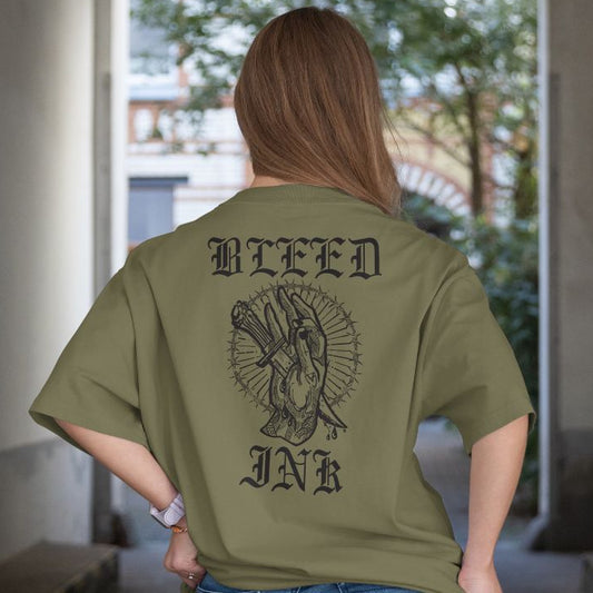 Person wearing a green t-shirt with 'BLEED INK' design on the back, standing indoors.