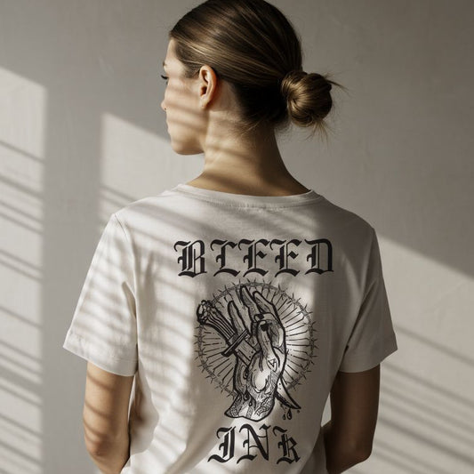 Close up
Person wearing a white t-shirt with 'BLEED INK' design on the back, standing against a neutral wall.