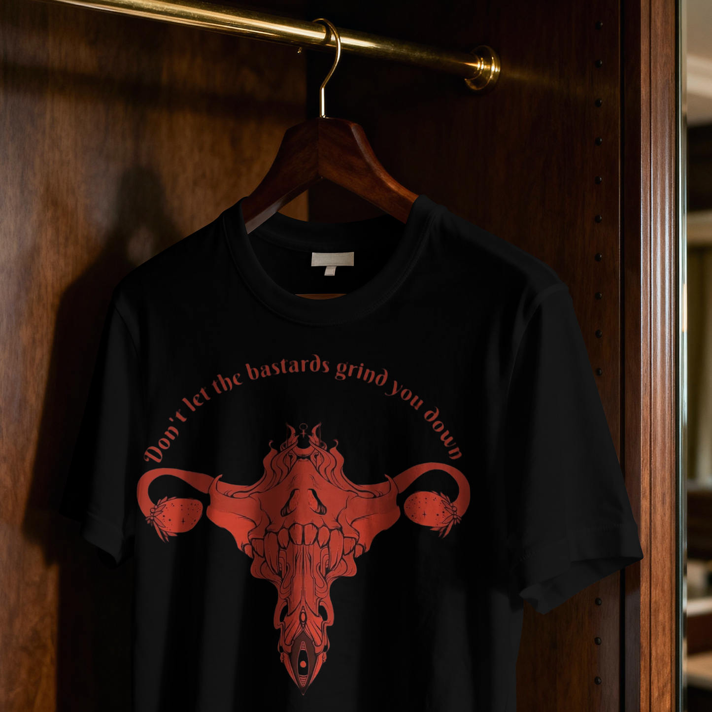 Black t-shirt with red graphic and text on a hanger against a wooden door.