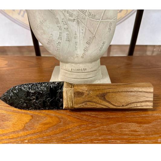 Close up
Decorative Obsidian knife, and wooden handle on a wooden surface, with a statue in the background.