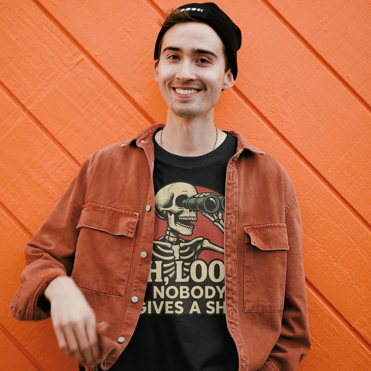 Person wearing a brown jacket and black t-shirt with a skeleton graphic against an orange wall