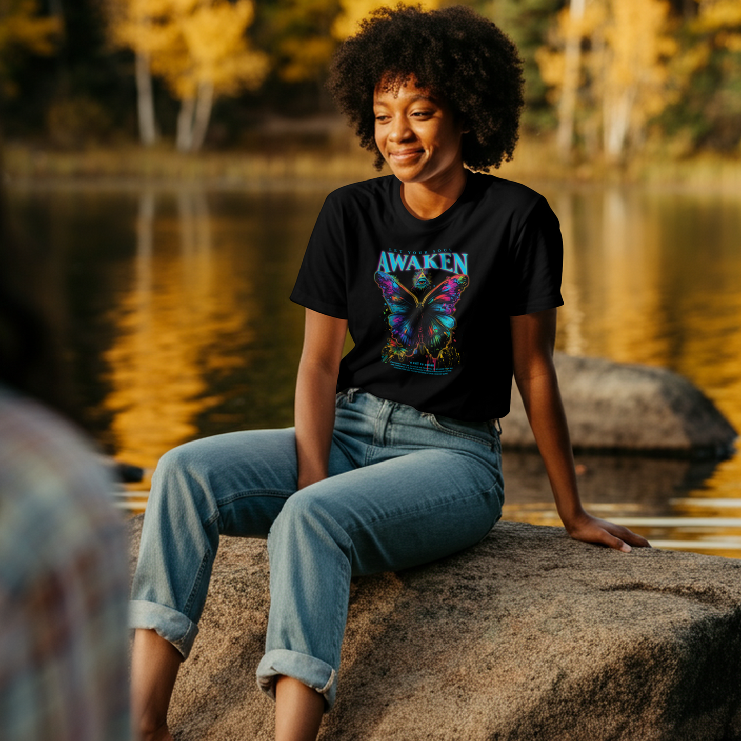 Person sitting on a rock by a lake with trees reflecting in the water