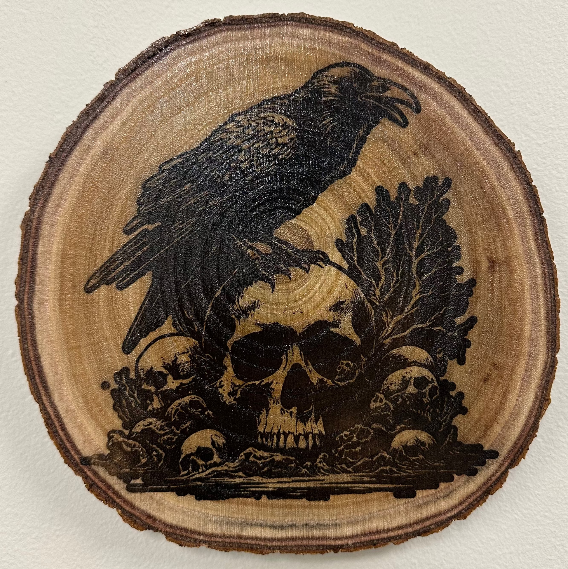 Close Up - Top View
Round - Wooden Plaque with a carved design of a crow and skulls on a light background. 