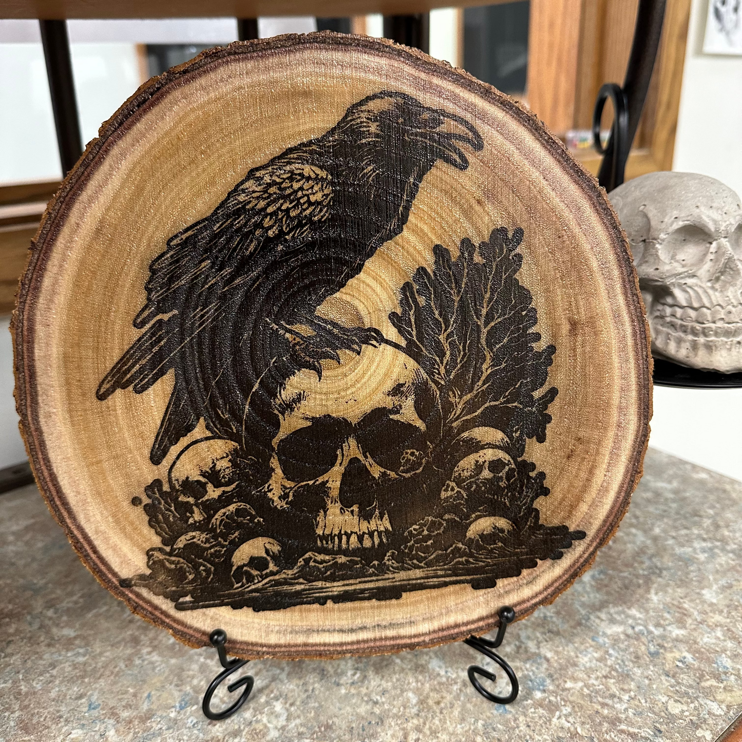 Close Up - Front View on a stand
Round - Wooden Wall-Hanger or Stand, with a carved design of a crow and skulls on a stand.