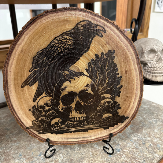Close Up - Front View on a stand
Round - Wooden Wall-Hanger or Stand, with a carved design of a crow and skulls on a stand.