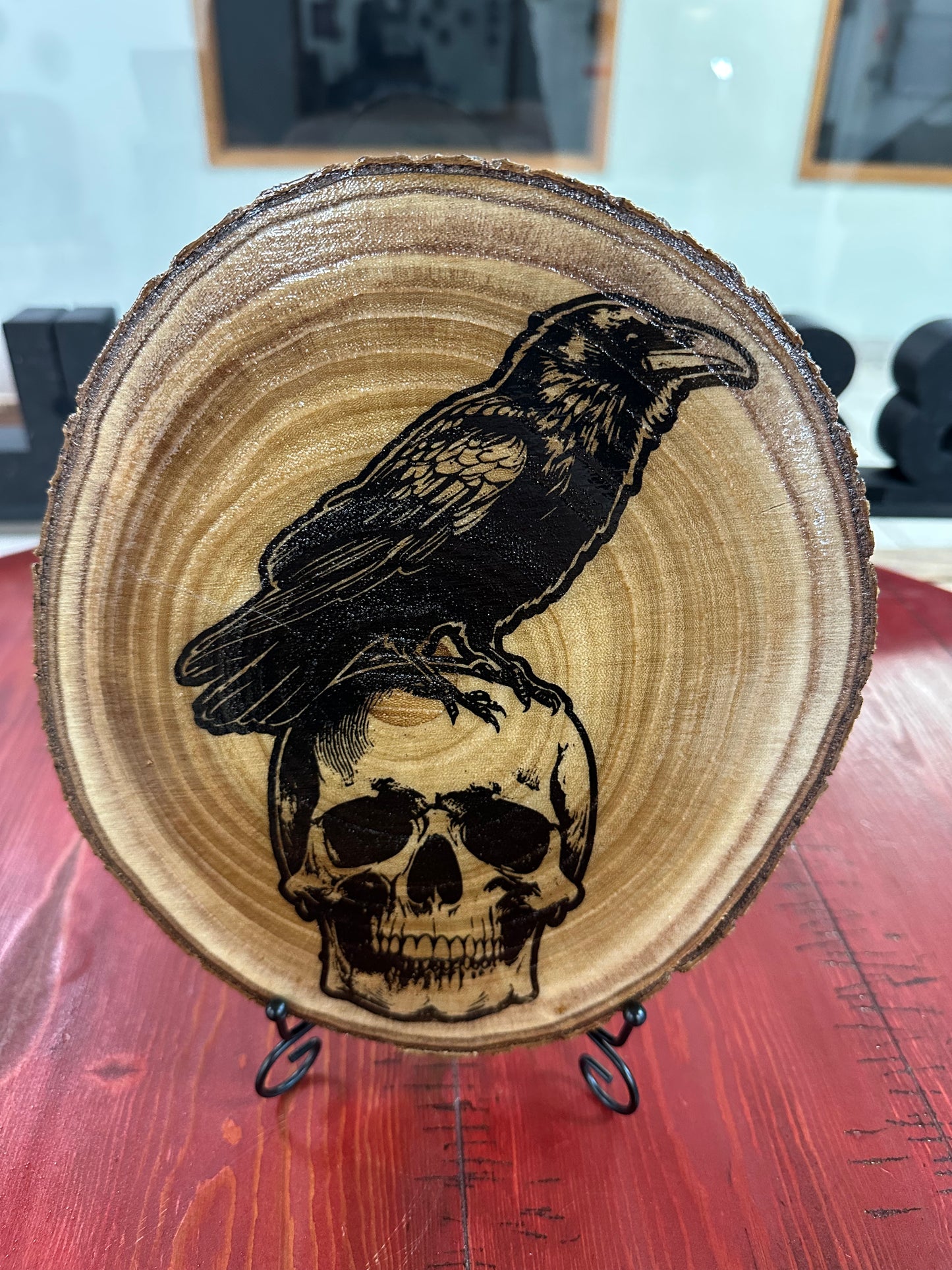 Close Up - Front view
Wood round with a engraved raven and skull design, sitting on a red surface.