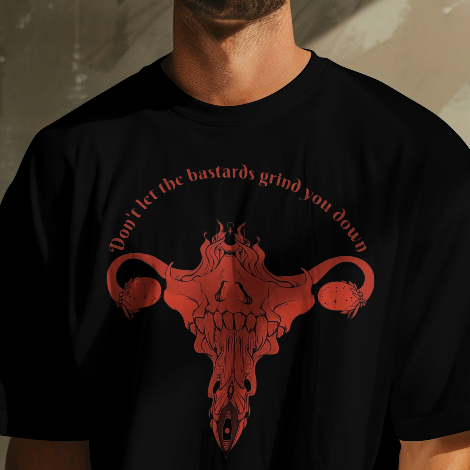 Black t-shirt with red graphic design and text worn by a person against a textured wall.