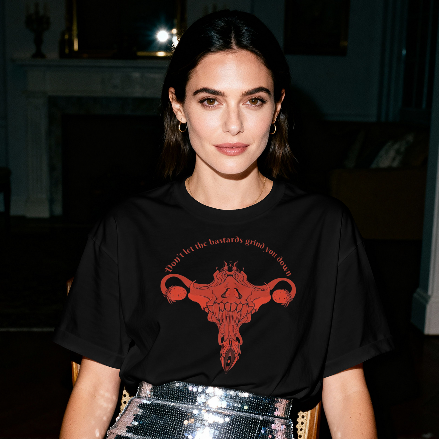 Woman wearing a black t-shirt with a red graphic design, sitting at a table in a dimly lit room.