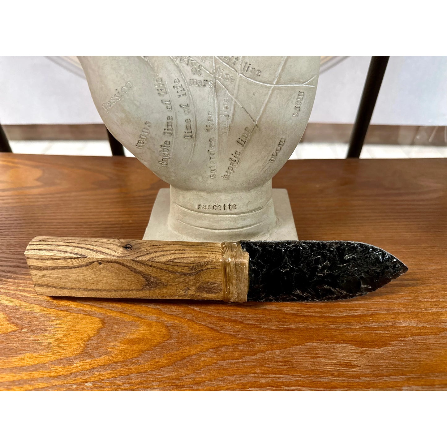 Decorative knife with wooden handle and black blade, on a wooden surface, with a statue in the background.