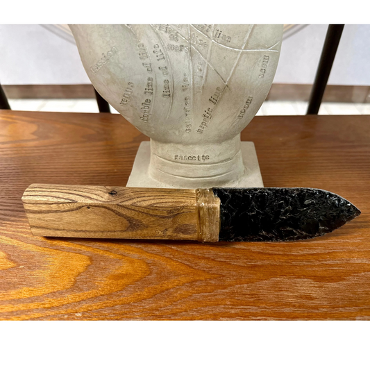 Decorative knife with wooden handle and black blade, on a wooden surface, with a statue in the background.