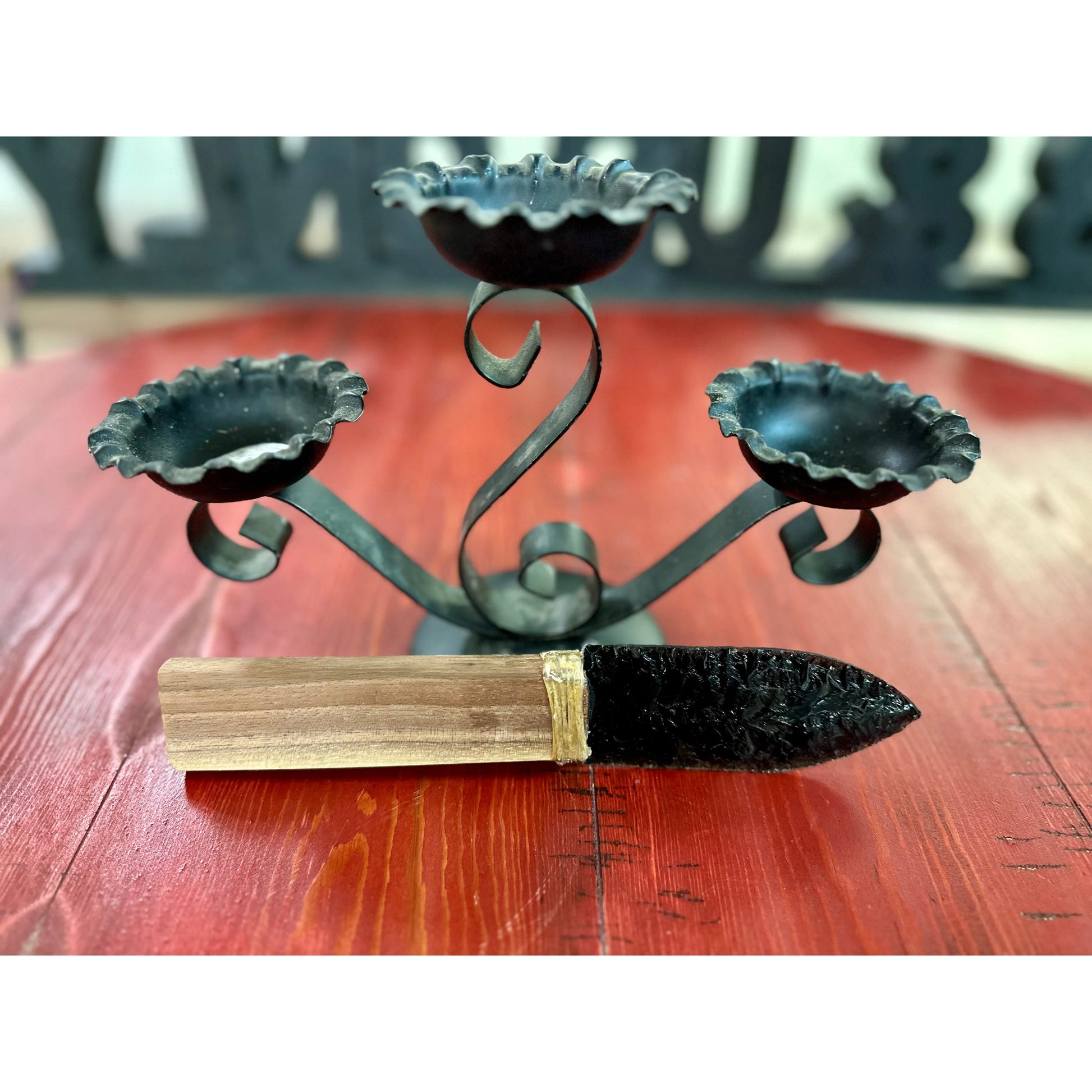 Obsidian knife decorative metal candle holder with three candle holders on a wooden surface.