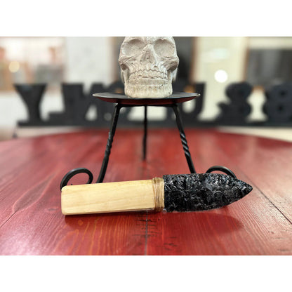 Decorative item with wooden handle and black decorative element on a red surface, skull in the background.