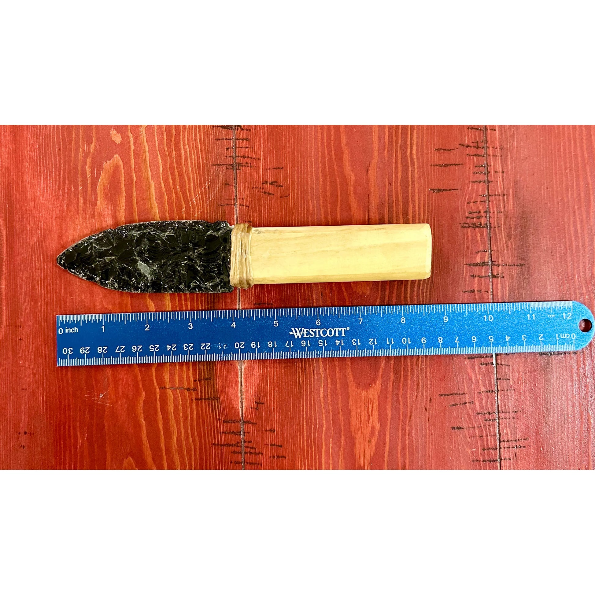 Hand made Obsidian knife  with wooden handle and stone head next to a ruler on a wooden surface