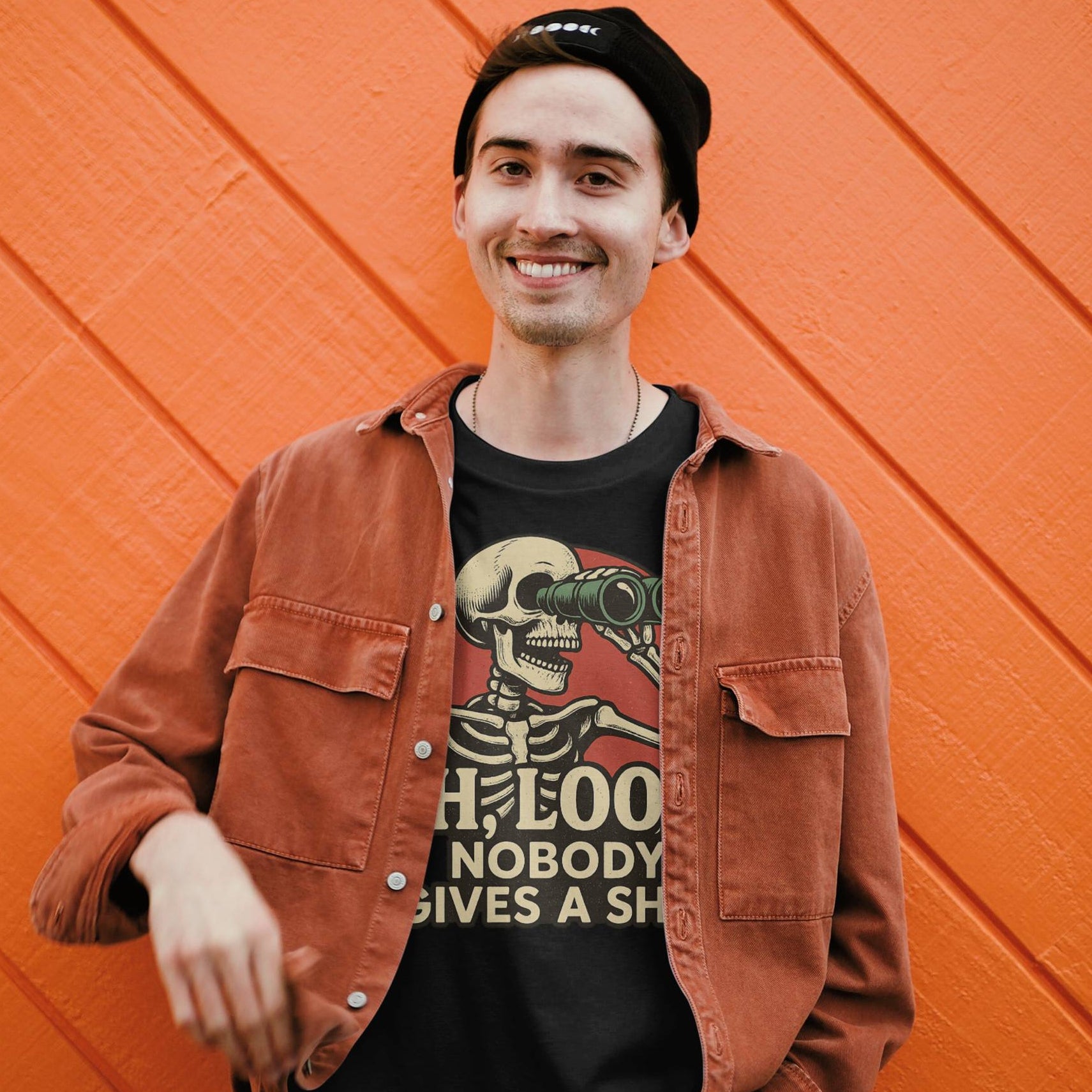 Person wearing a brown jacket and black t-shirt with a skeleton graphic against an orange wall