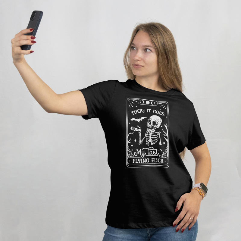 Woman wearing a black t-shirt with graphic design and text, taking a selfie against a plain background