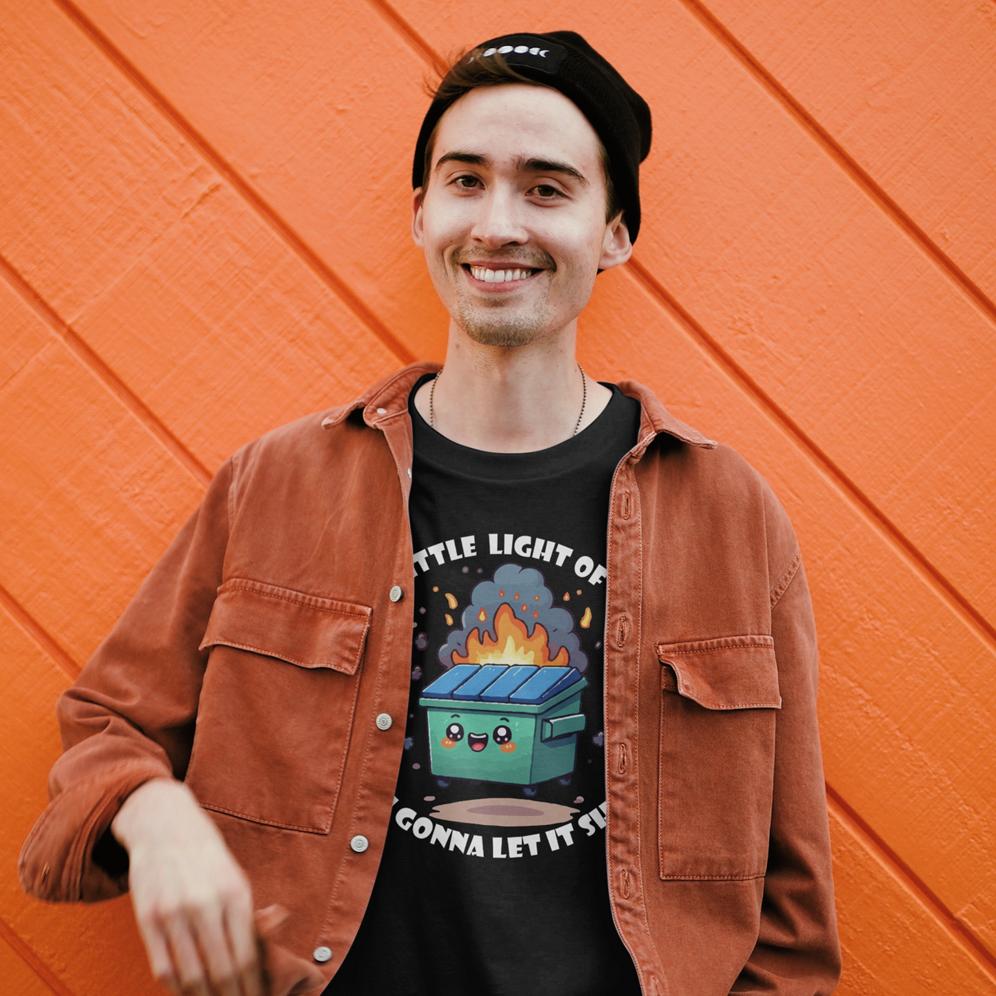 Person wearing a black t-shirt with a graphic design and an orange jacket, standing against an orange wall.