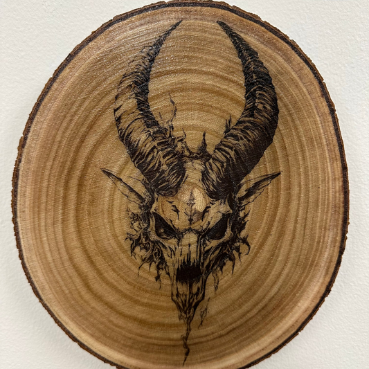 Close Up - Top View
Round-Wooden plaque with a black ink drawing of a goat skull with horns on a white background