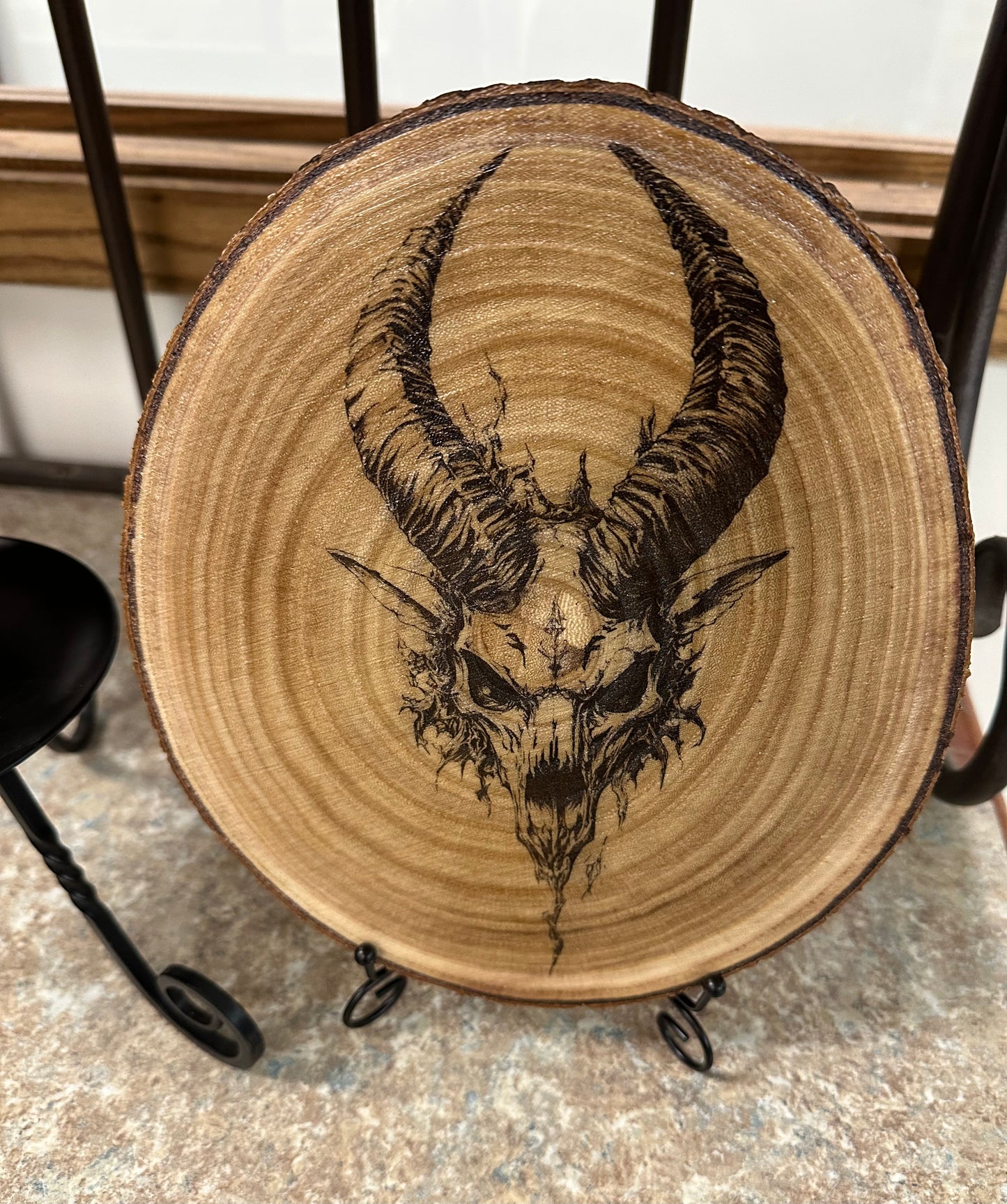 Wooden round piece with a black ink drawing of a goat skull and horns on a metal stand.