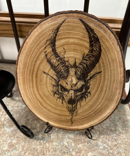 Wooden round piece with a black ink drawing of a goat skull and horns on a metal stand.