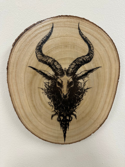 Wooden plaque with a black ink drawing of a goat head with large horns on a white background