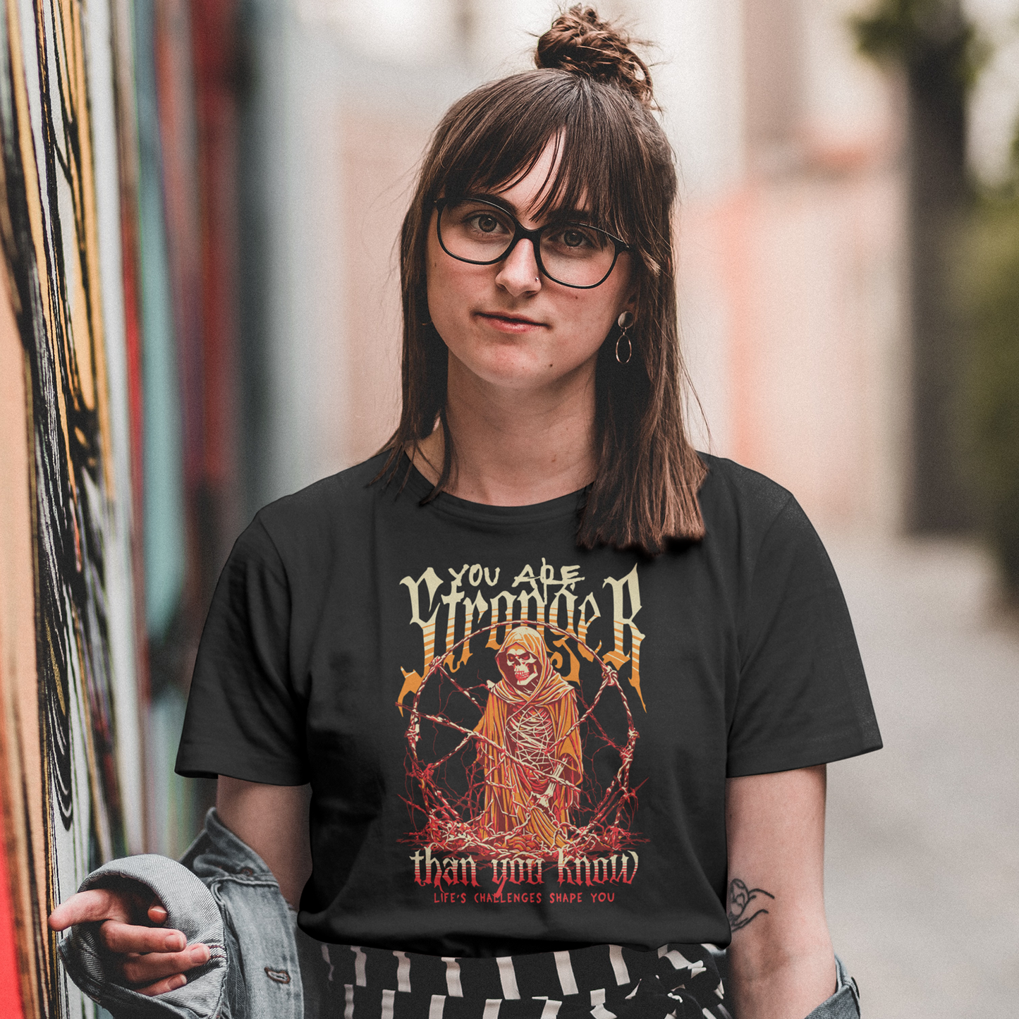Person wearing a black t-shirt with a graphic design and text, standing in an alleyway.